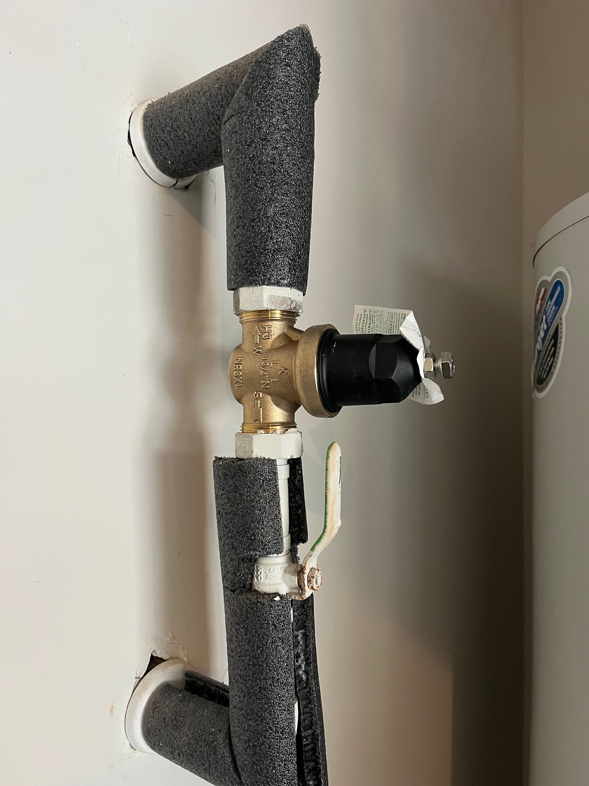 A close up of a water heater valve on a wall.
