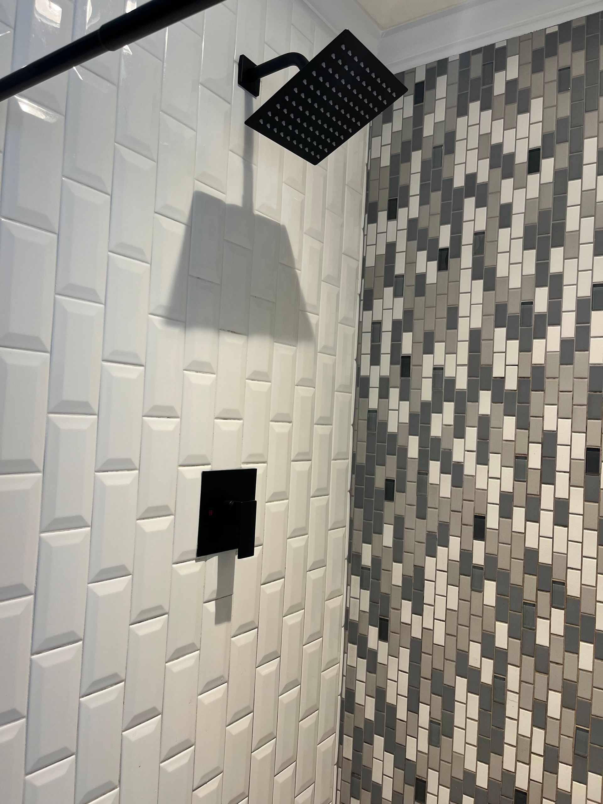 A shower with white tiles and a black shower head