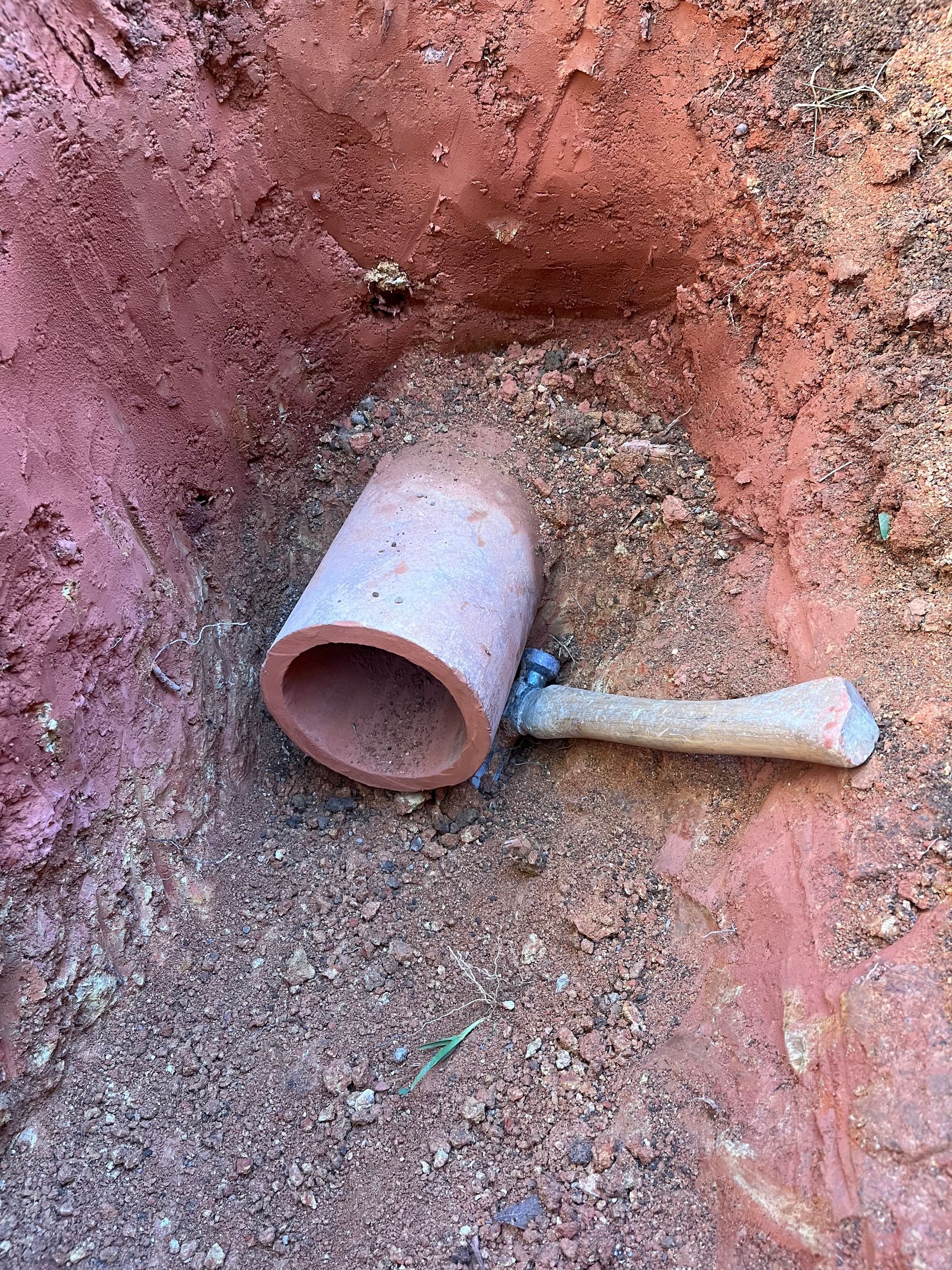 A hammer is laying in the dirt next to a pipe.