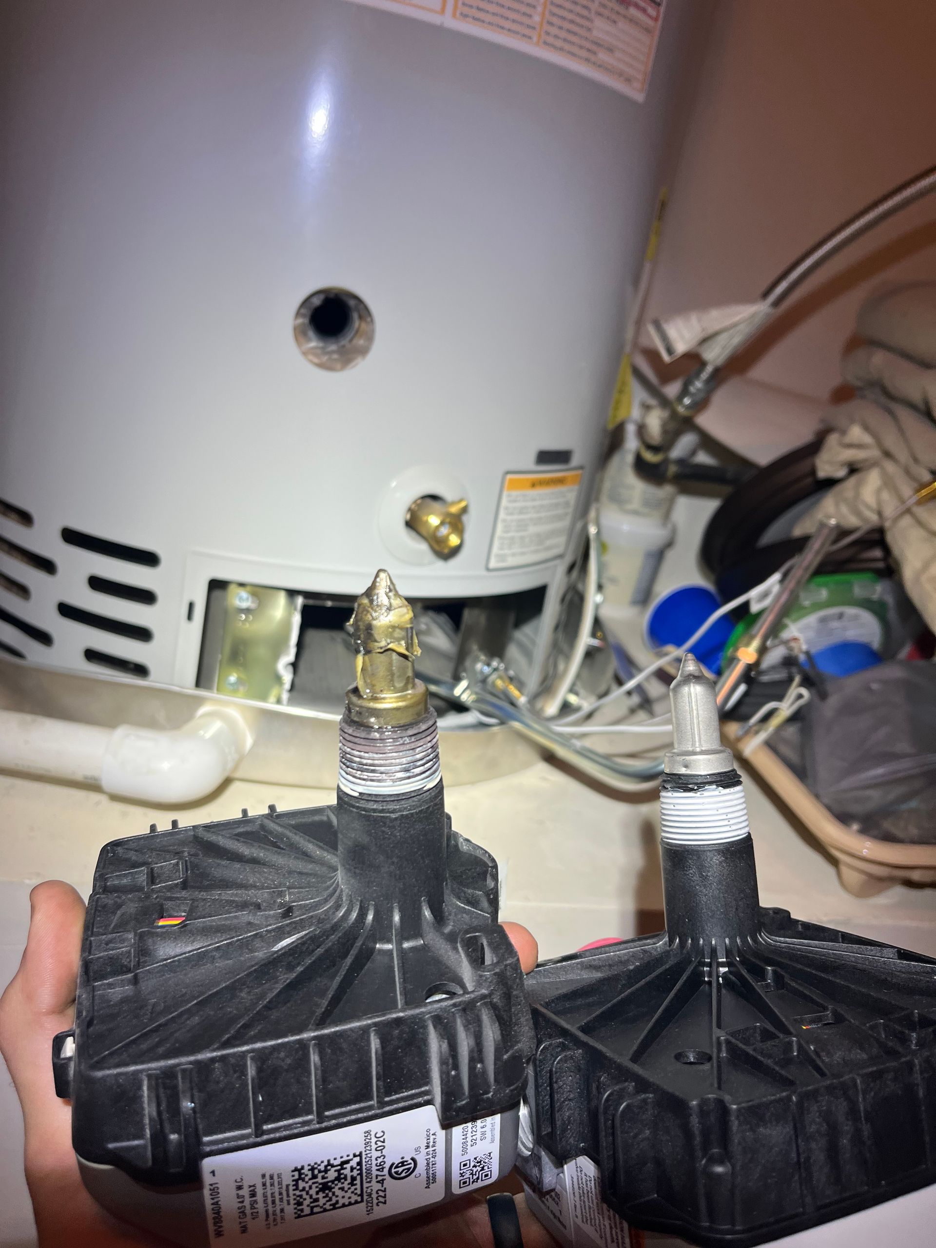 A person is holding two pieces of equipment in front of a water heater