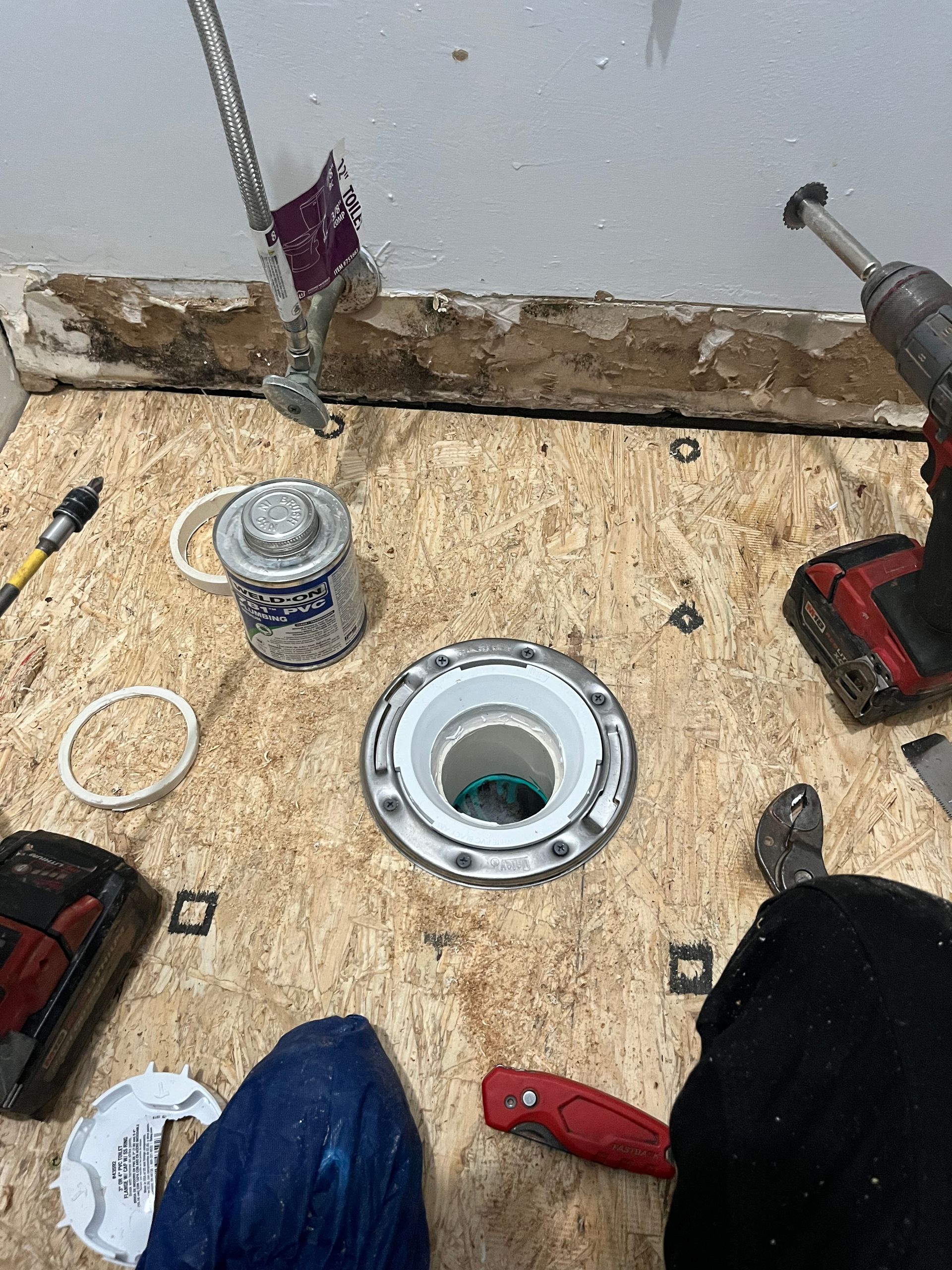 A person is using a drill to install a toilet flange.