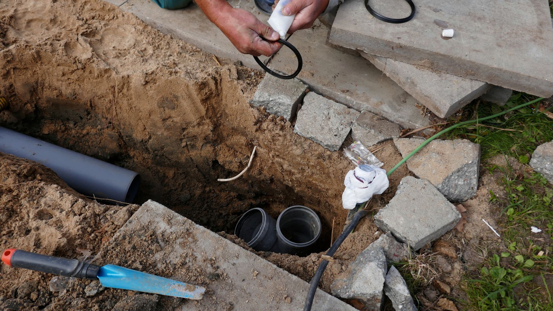 A man is fixing a pipe in a hole in the ground.