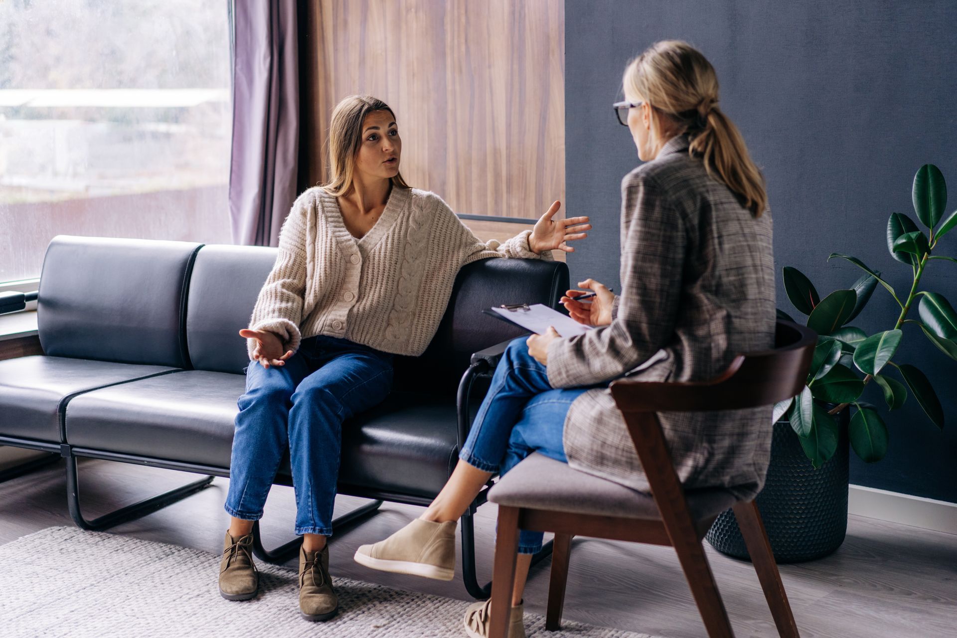 A woman is sitting on a couch talking to another woman.