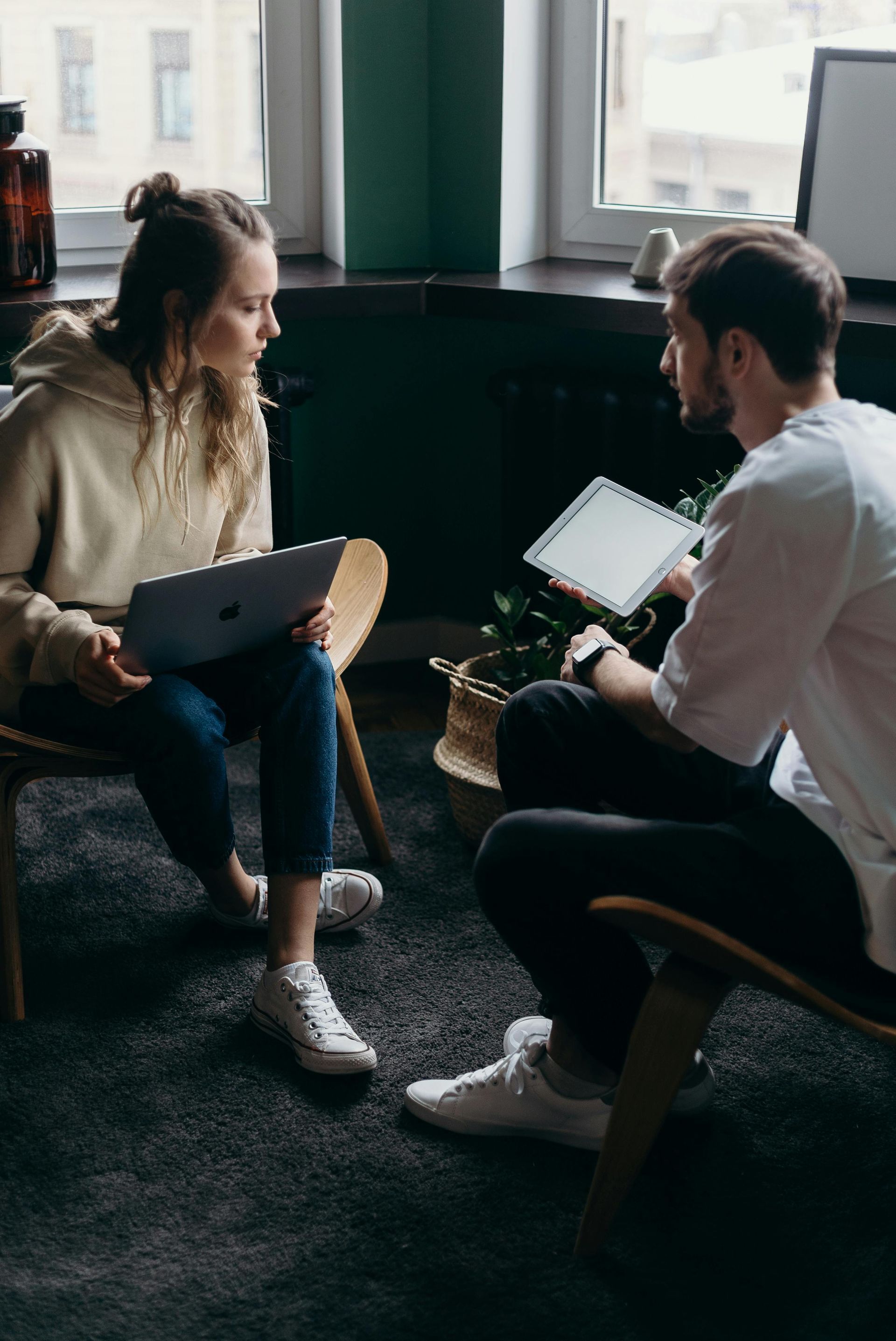 A man and a woman are sitting in chairs talking to each other . the woman is holding a tablet.