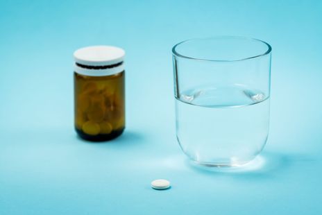 A bottle of pills and a glass of water on a blue background.