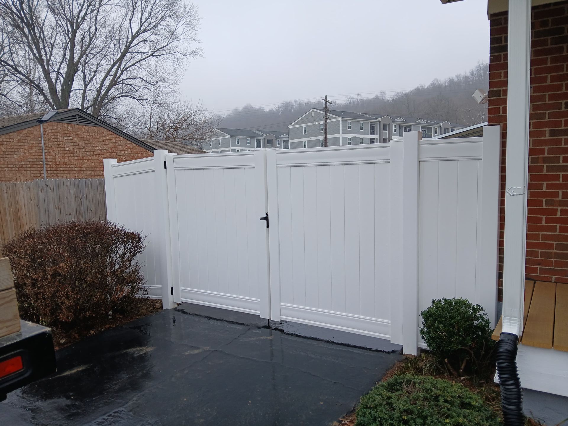 White vinyl fence with gate in front of a building on a cloudy day.