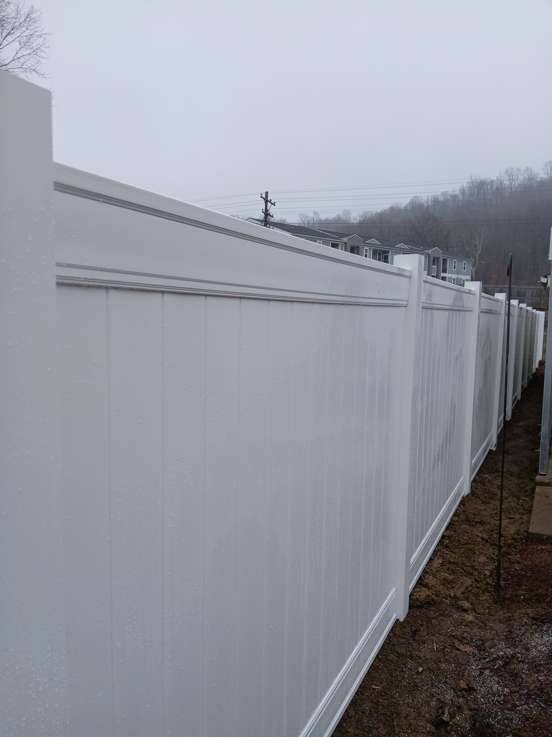 White vinyl privacy fence in a residential area on a cloudy day.