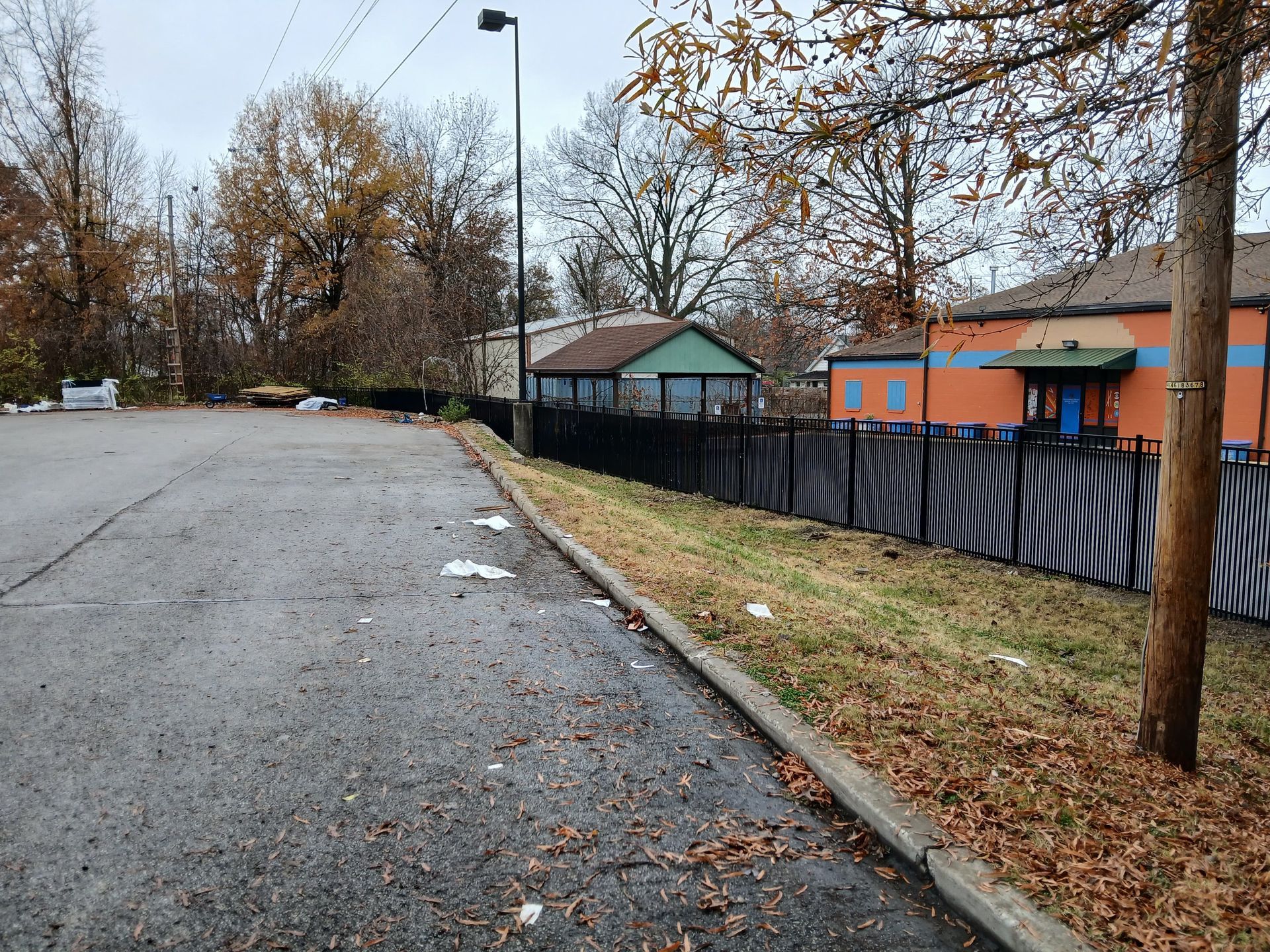 Quiet roadside with wooden fence, grassy verge, gravel path, and houses under trees on a sunny day