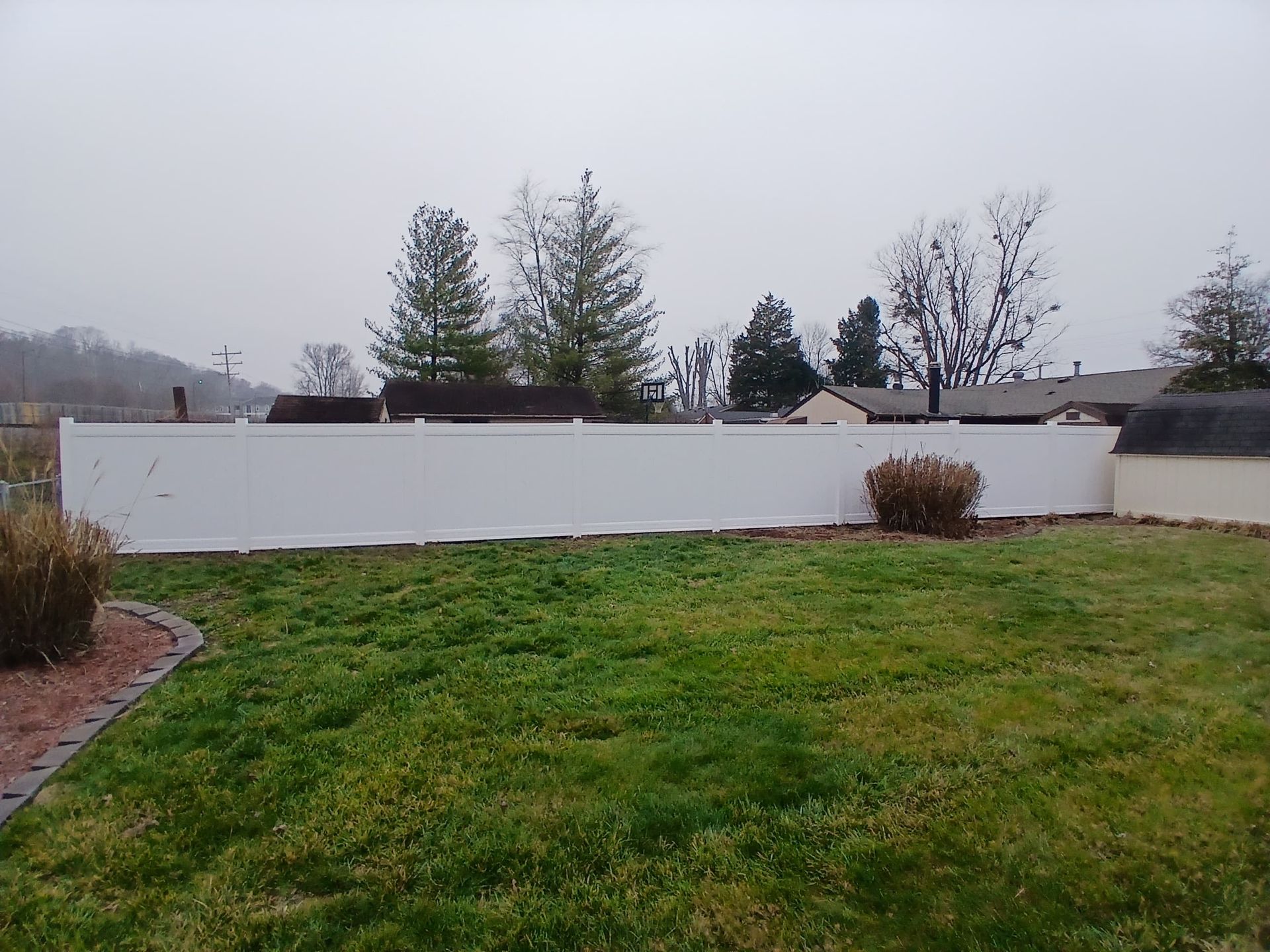 A white privacy fence in a backyard, with trees and a cloudy sky in the background.