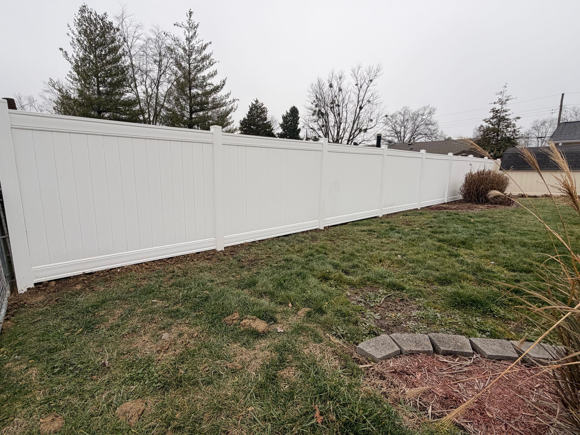 White vinyl fence in a grassy yard under an overcast sky.