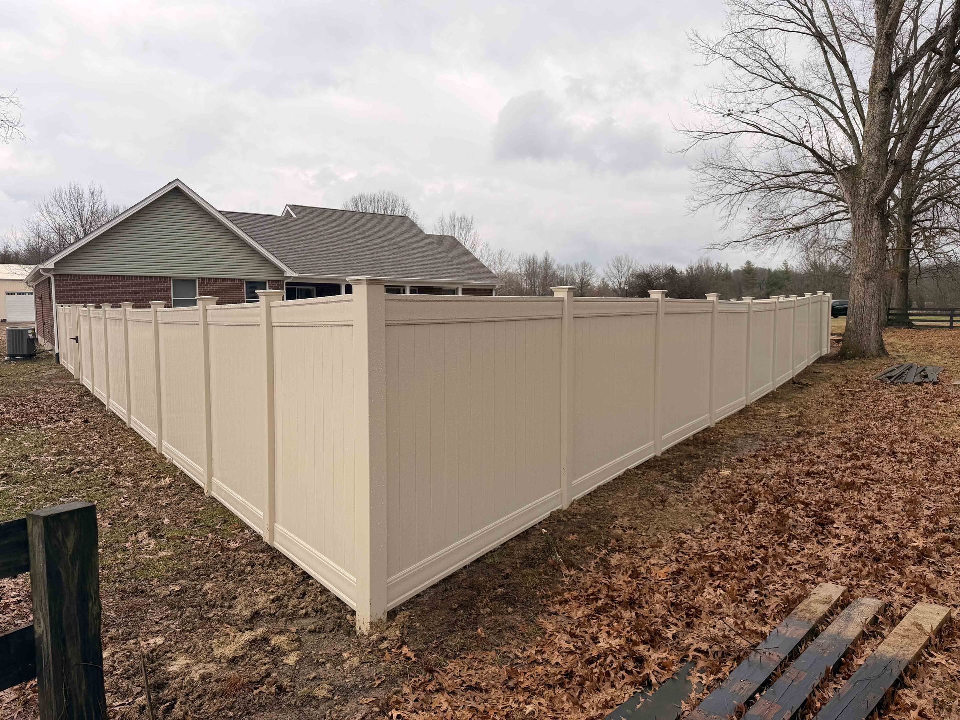 Tan vinyl fence surrounding a house and yard on a cloudy day.