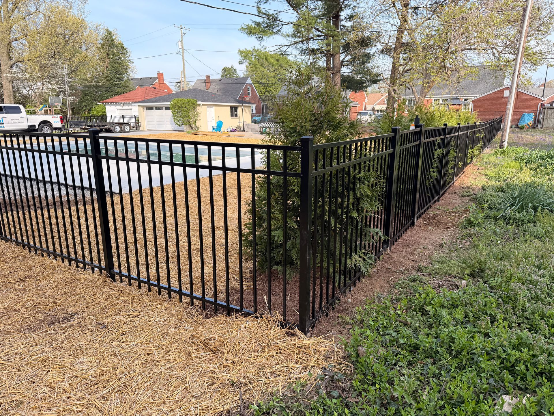Black metal fence beside a gravel path and trimmed greenery in a suburban neighborhood