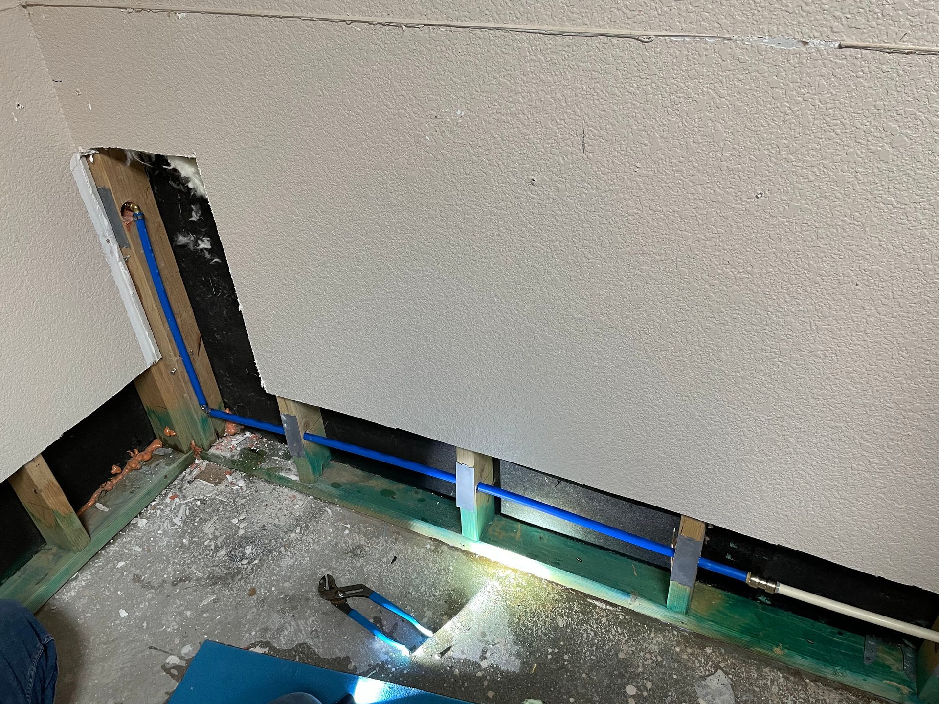 A person is working on a wall with blue pipes coming out of it.