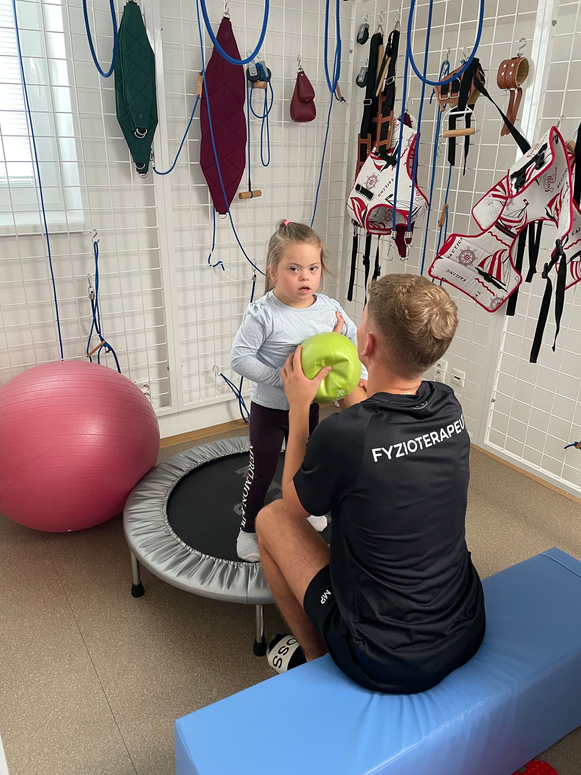 A young girl with Down syndrome exercises with a physical therapist, using a skull prop and a trampoline.