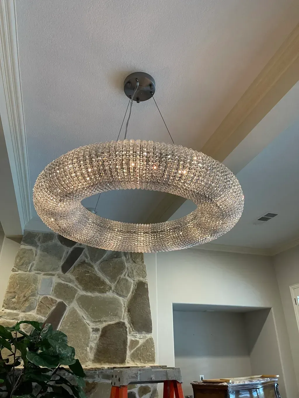 Circular crystal chandelier hangs from ceiling, over stone fireplace.