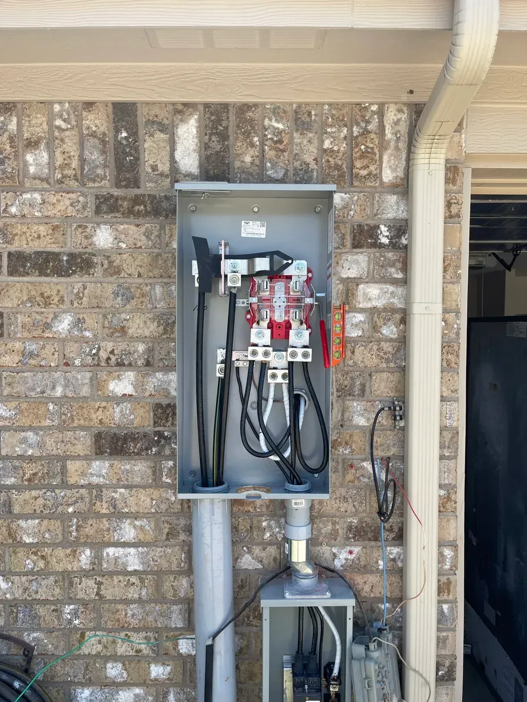 Electrical meter box attached to a brick wall, with wires and a visible meter inside.