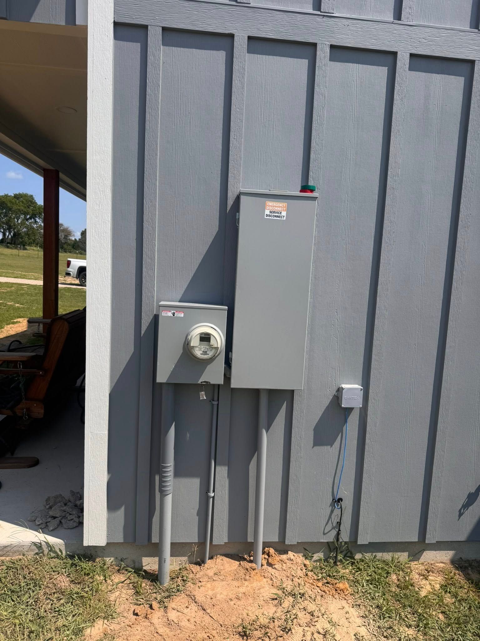 Electrical panel and meter box on a gray building's exterior wall, with conduits running to the ground.