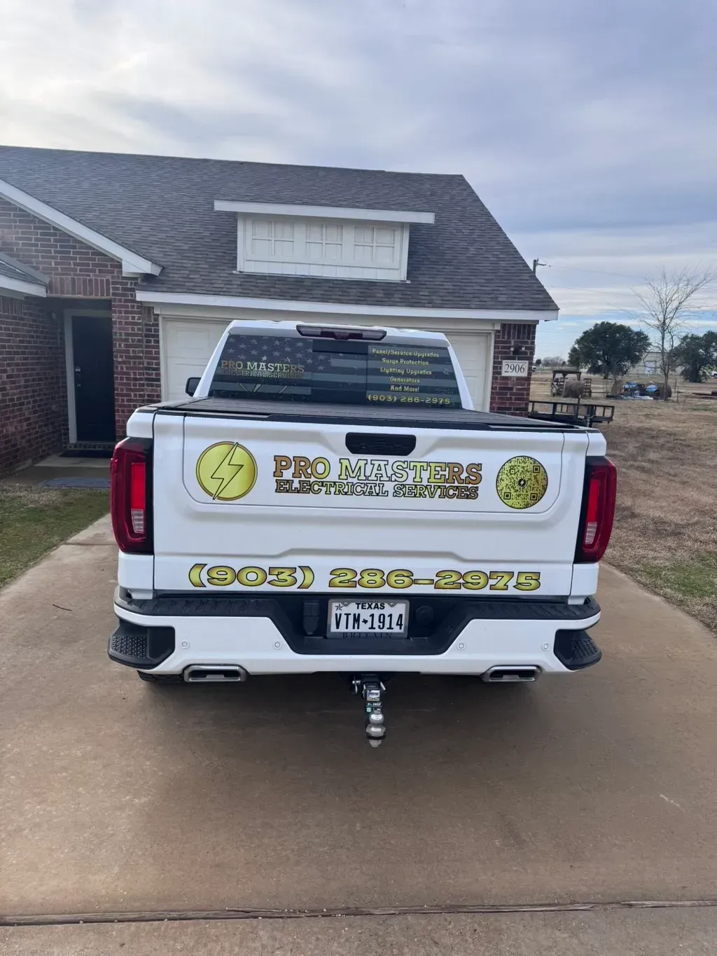 White pickup truck with business logos and phone number parked in front of a house.
