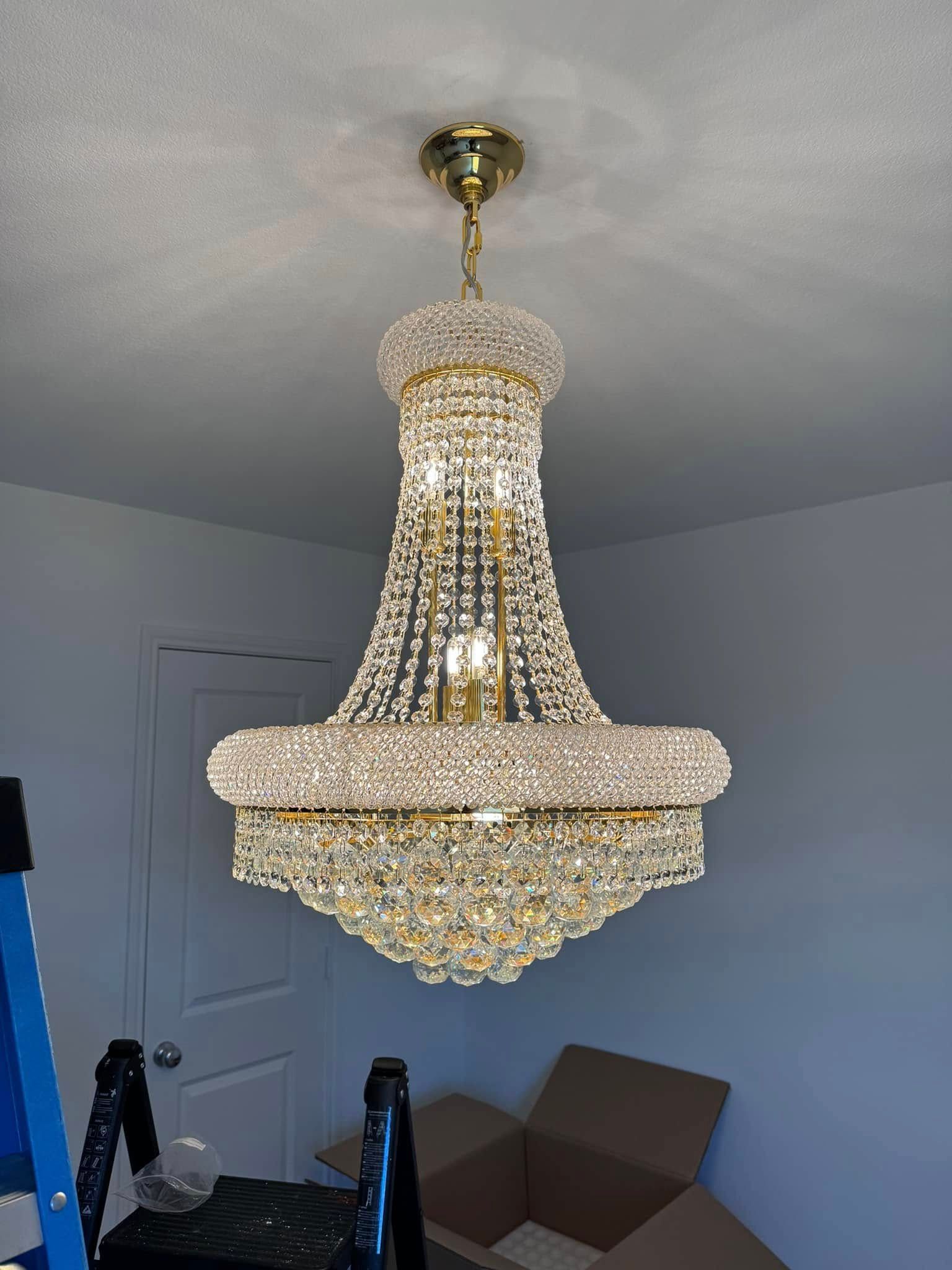 Gold and crystal chandelier hanging from a white ceiling in a room, a ladder is on the left.
