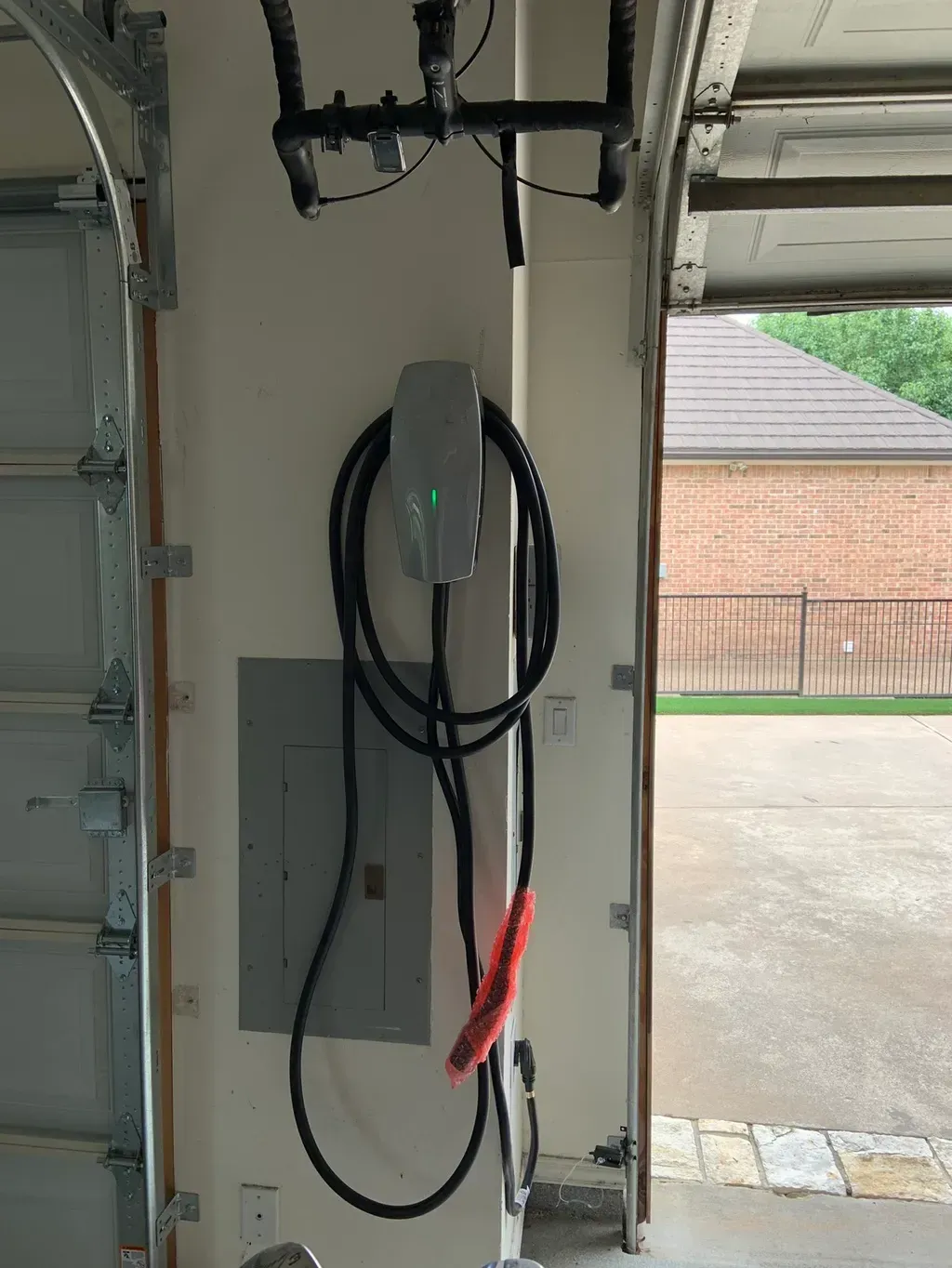 EV charger installed in a garage next to the electrical panel, cable hanging down.