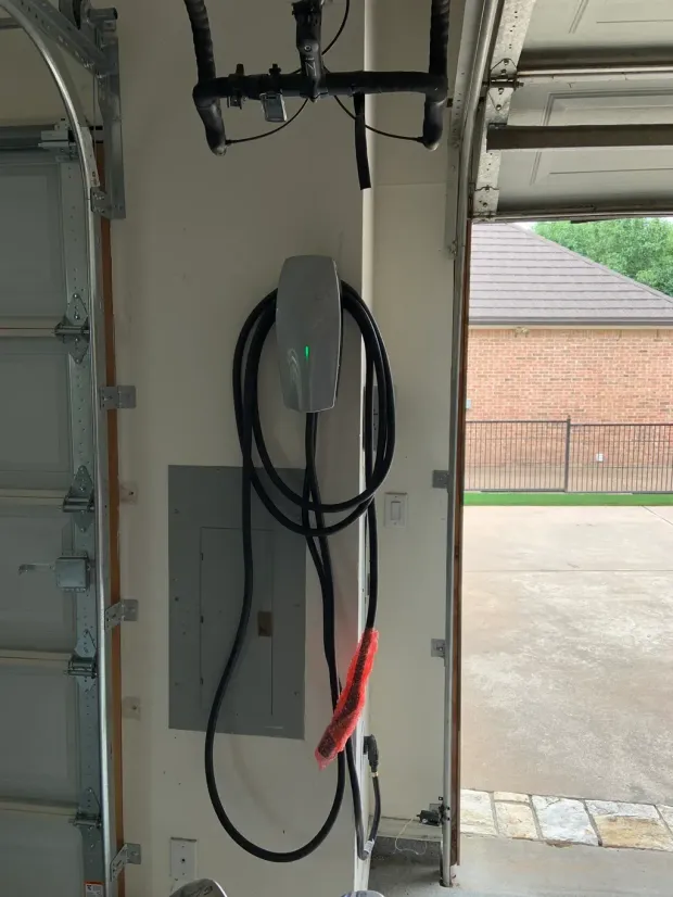 Electric vehicle charger next to electrical panel inside a garage.