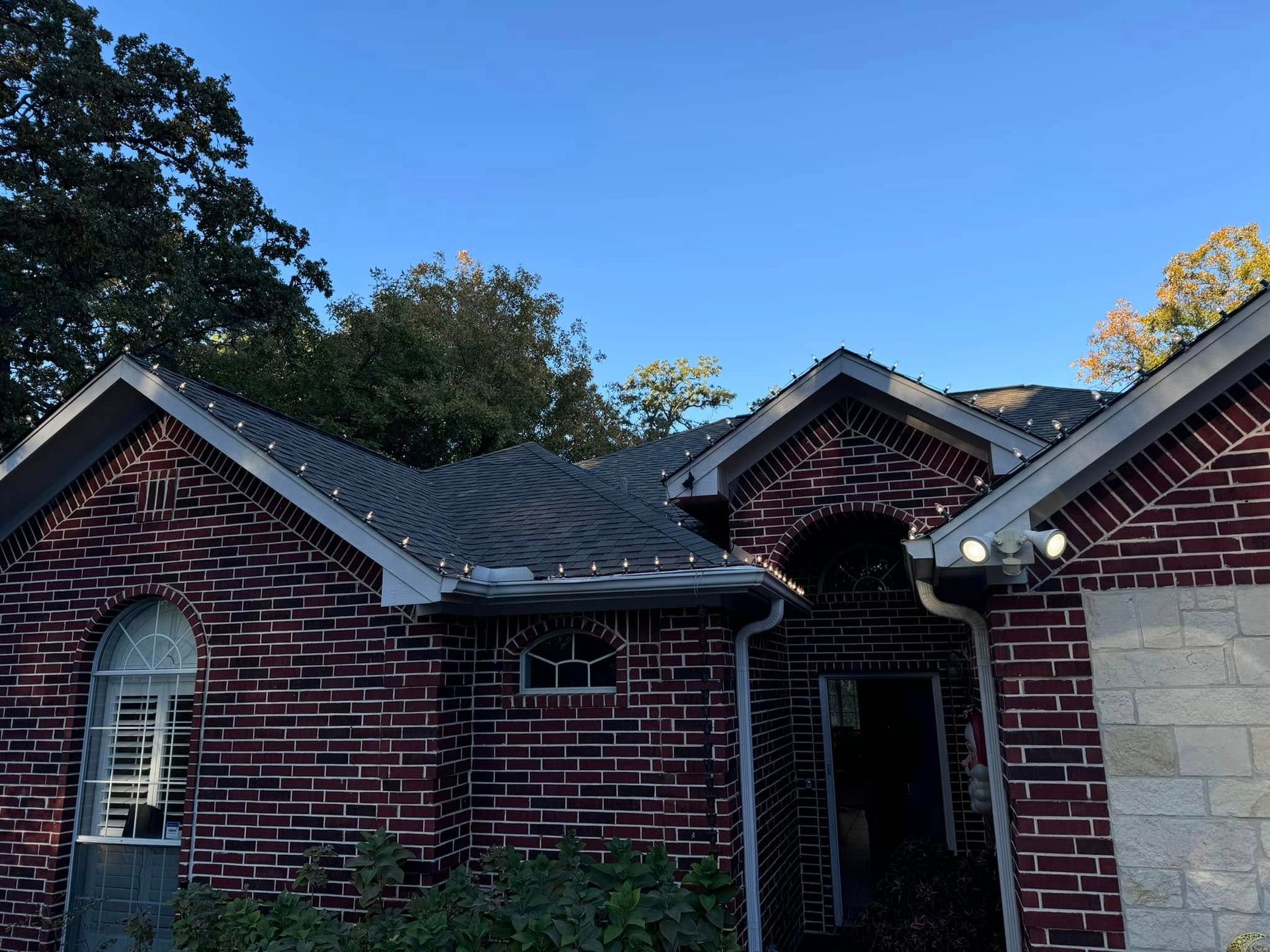 Brick house with Christmas lights along the roofline under a blue sky.