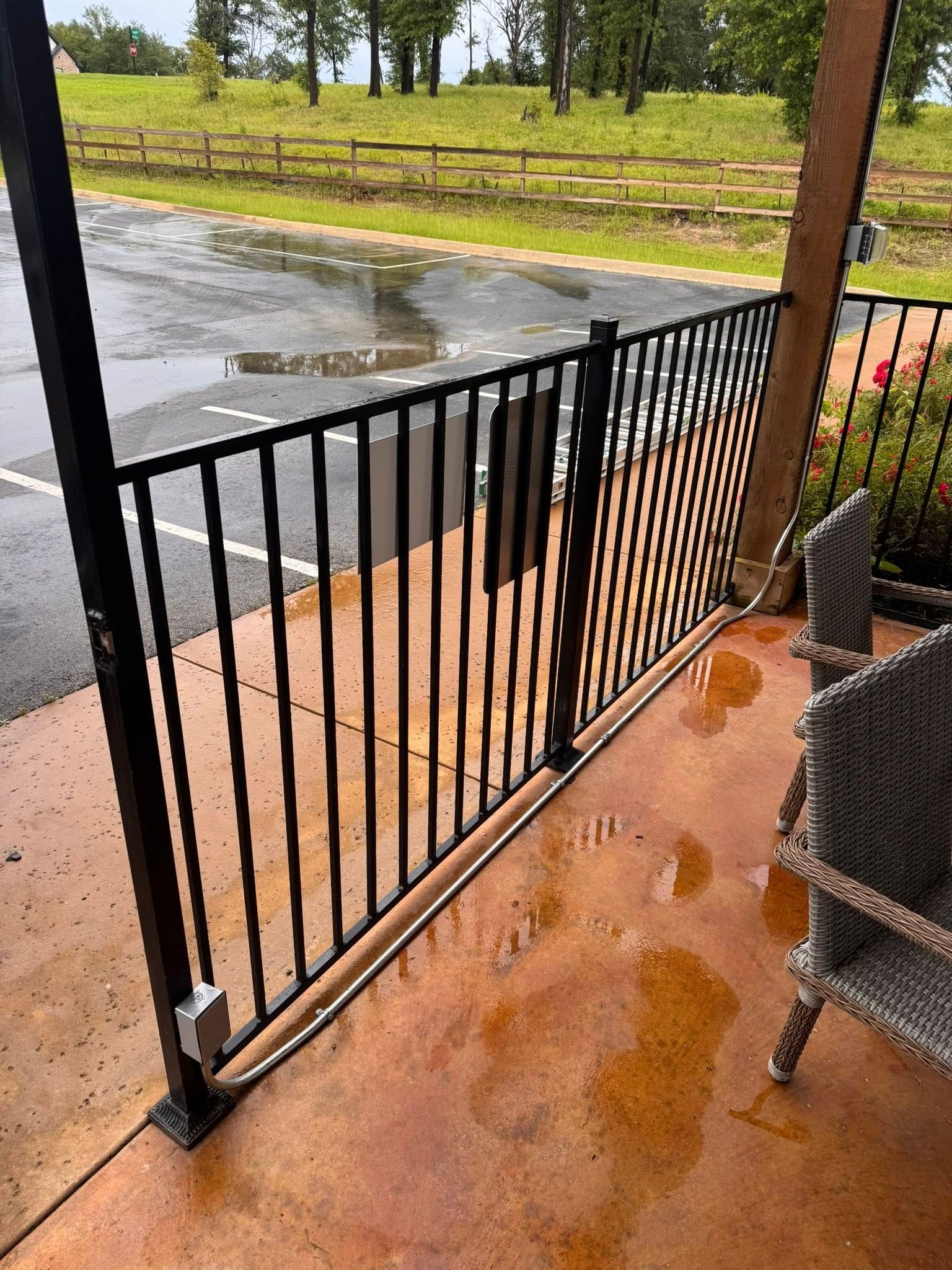 Black metal fence on a wet, reddish-brown patio. A wicker chair sits nearby.