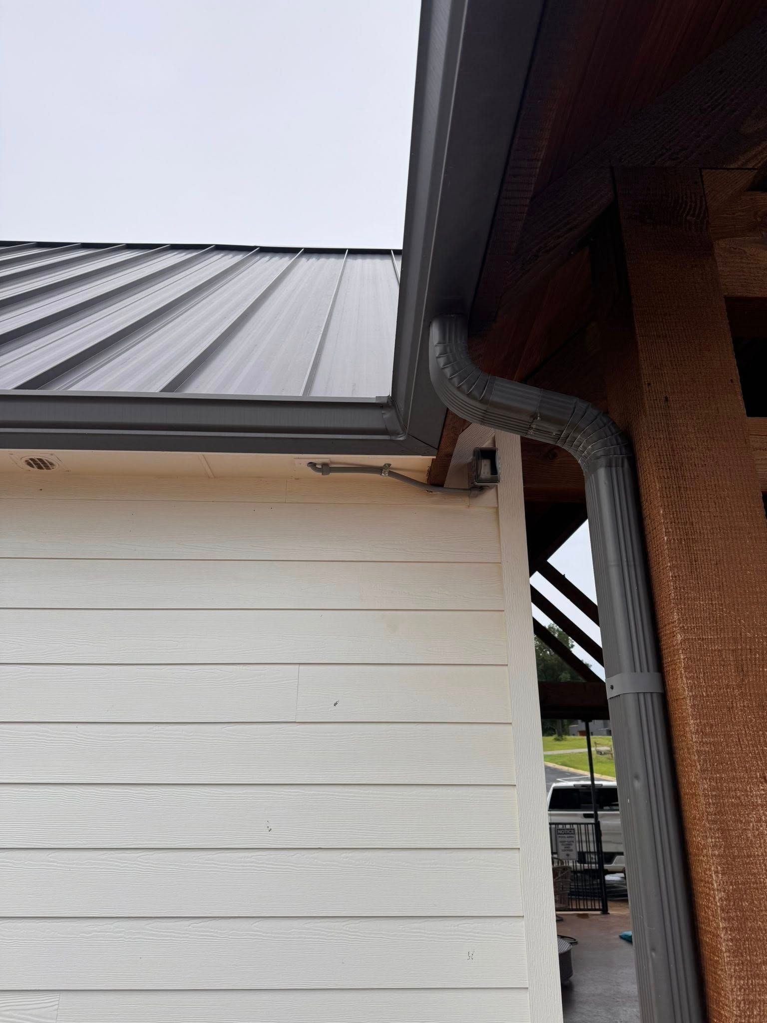 Corner of a building with a black metal roof, gray gutters, and white siding.