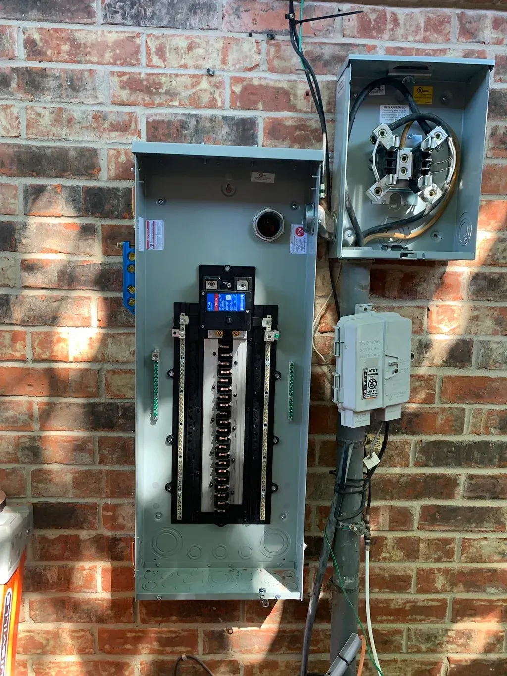 Exterior electrical panel mounted on a brick wall, including a meter and circuit breaker box.