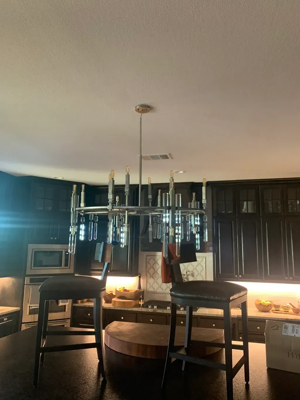 Kitchen with chandelier, dark cabinets, two bar stools, and a central island.