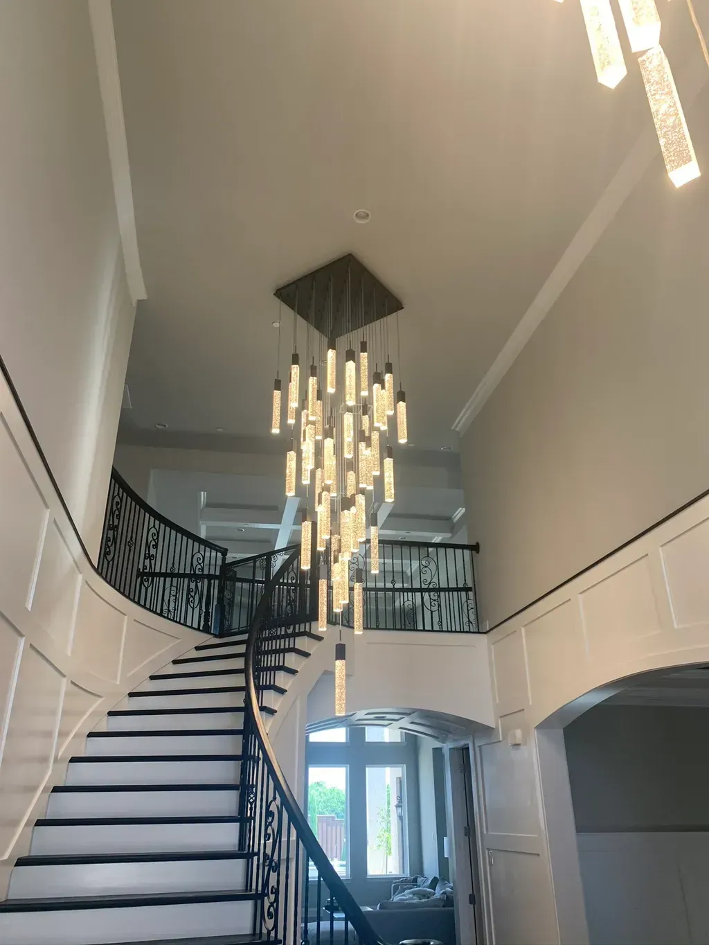 A grand staircase in a home with a chandelier, dark banister, and white walls.