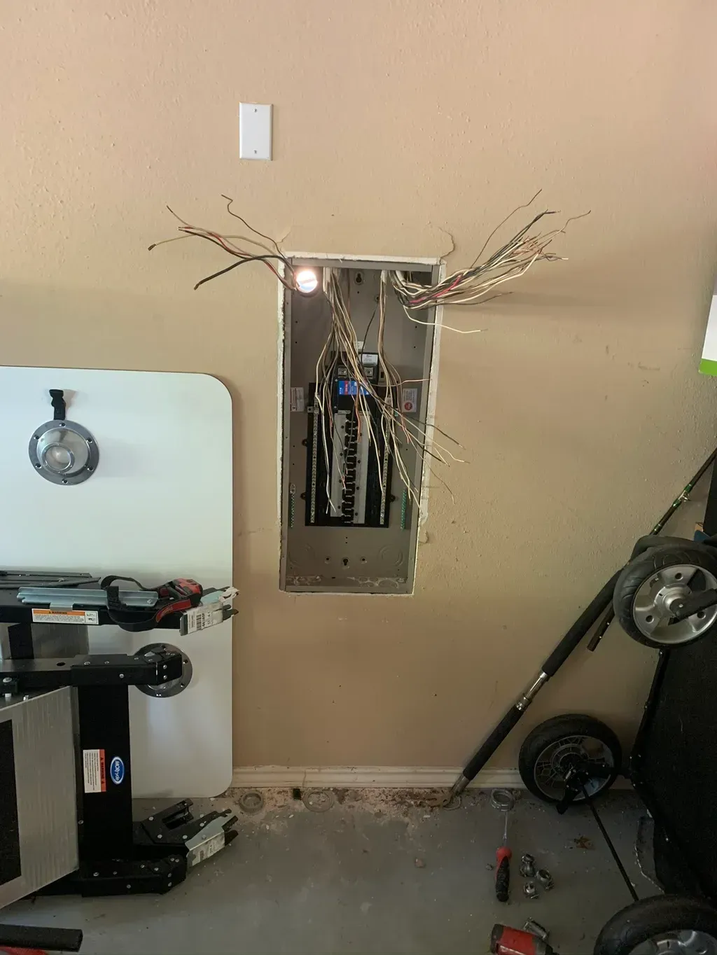 Electrical panel in garage with wires exposed.