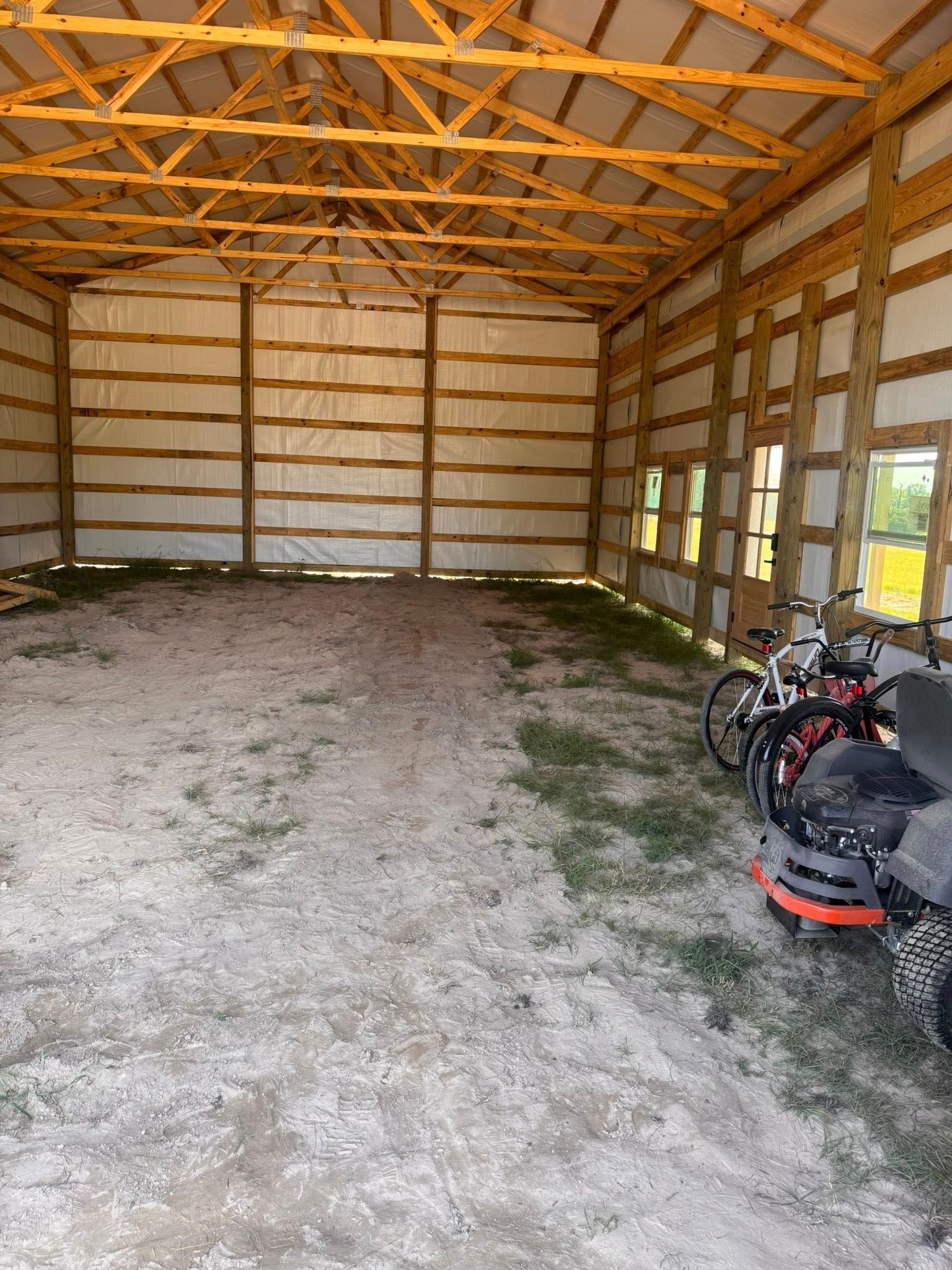 Empty barn interior with gravel floor, wooden beams, and some bicycles.
