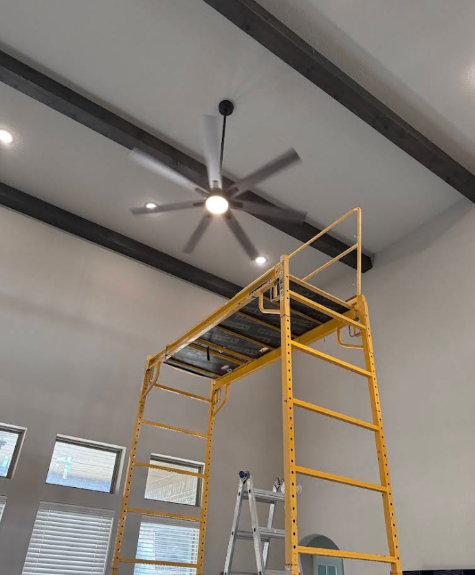 Yellow scaffold under a ceiling fan, in a room with beams.