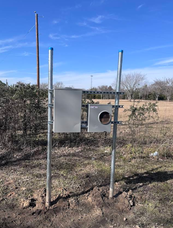 Metal utility boxes on posts in a grassy field under a blue sky.