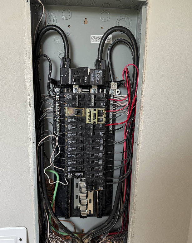 Electrical panel with black wires, circuit breakers, and red and white wires within a wall.