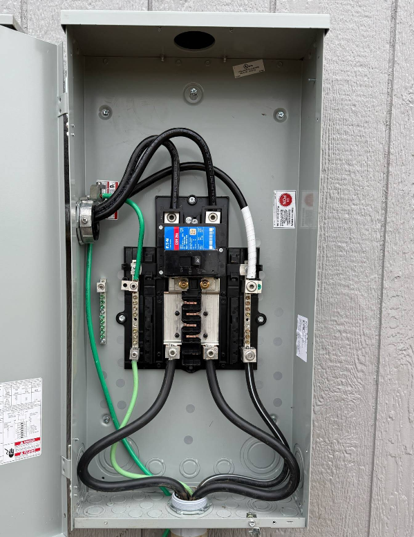 Gray electrical meter box, interior view. Black and green wires connected to a circuit breaker.