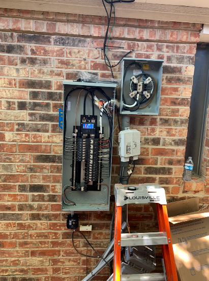 Electrical panel installed on a red brick wall, with a ladder below.