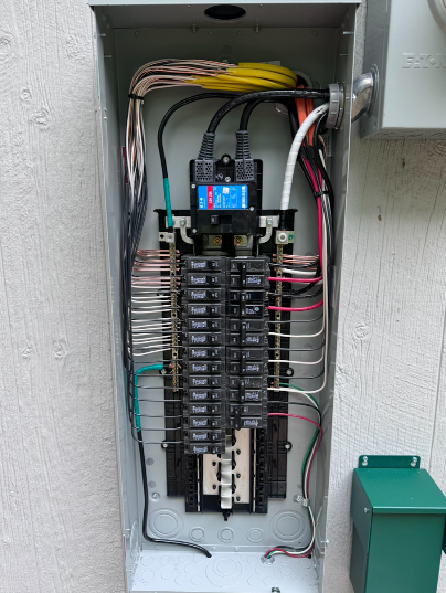 Electrical panel with black circuit breakers and connected wires inside a metal box on a wall.