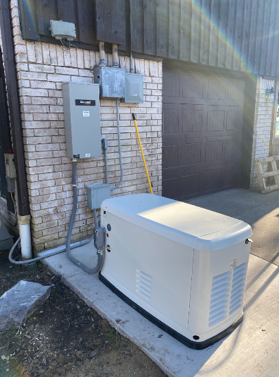 Exterior view: A beige generator next to a brick wall and a garage door. Electrical boxes are mounted on the wall.