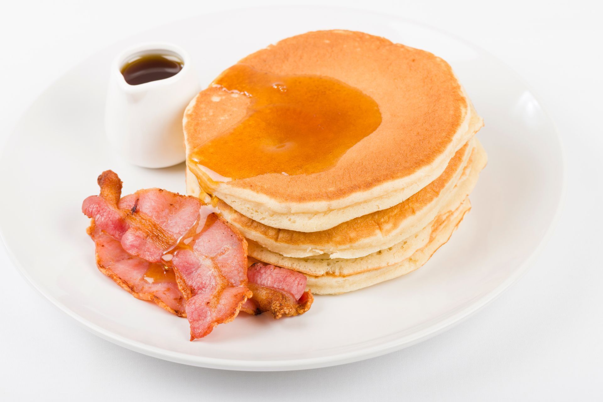 A white plate topped with pancakes bacon and syrup