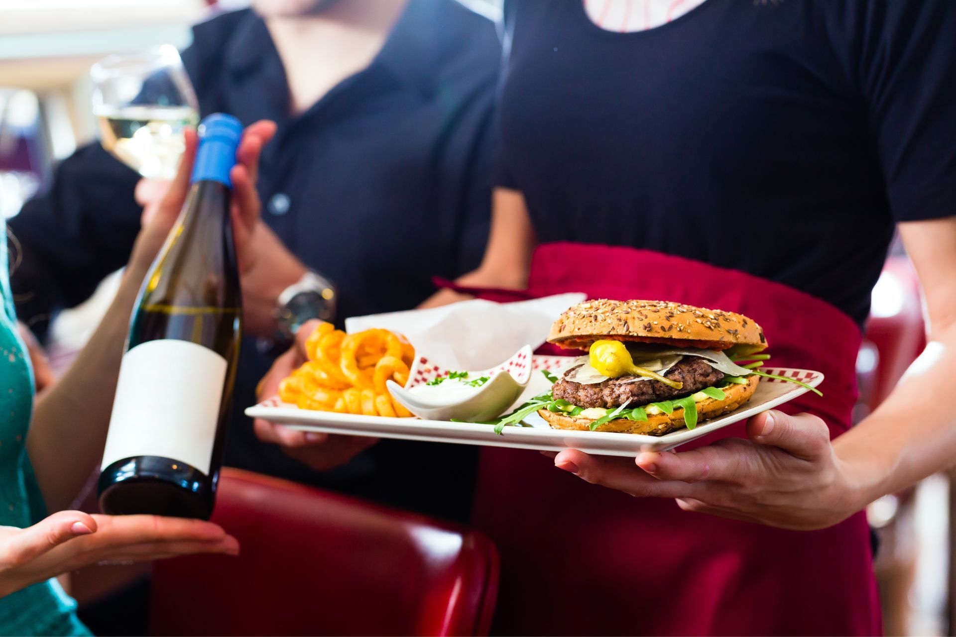 A waitress is holding a plate of food and a bottle of wine.