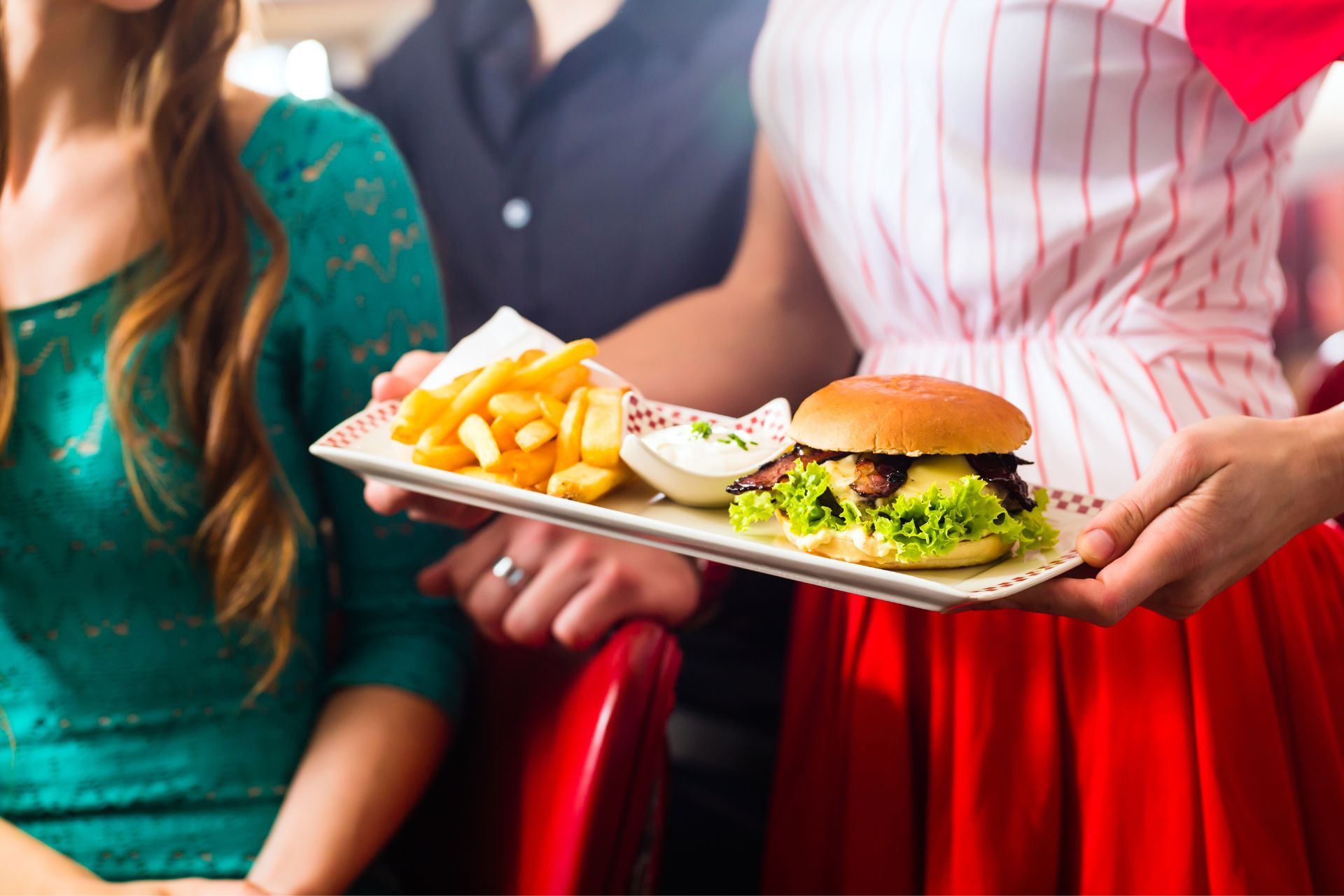 A woman is holding a plate of food with a hamburger and french fries.