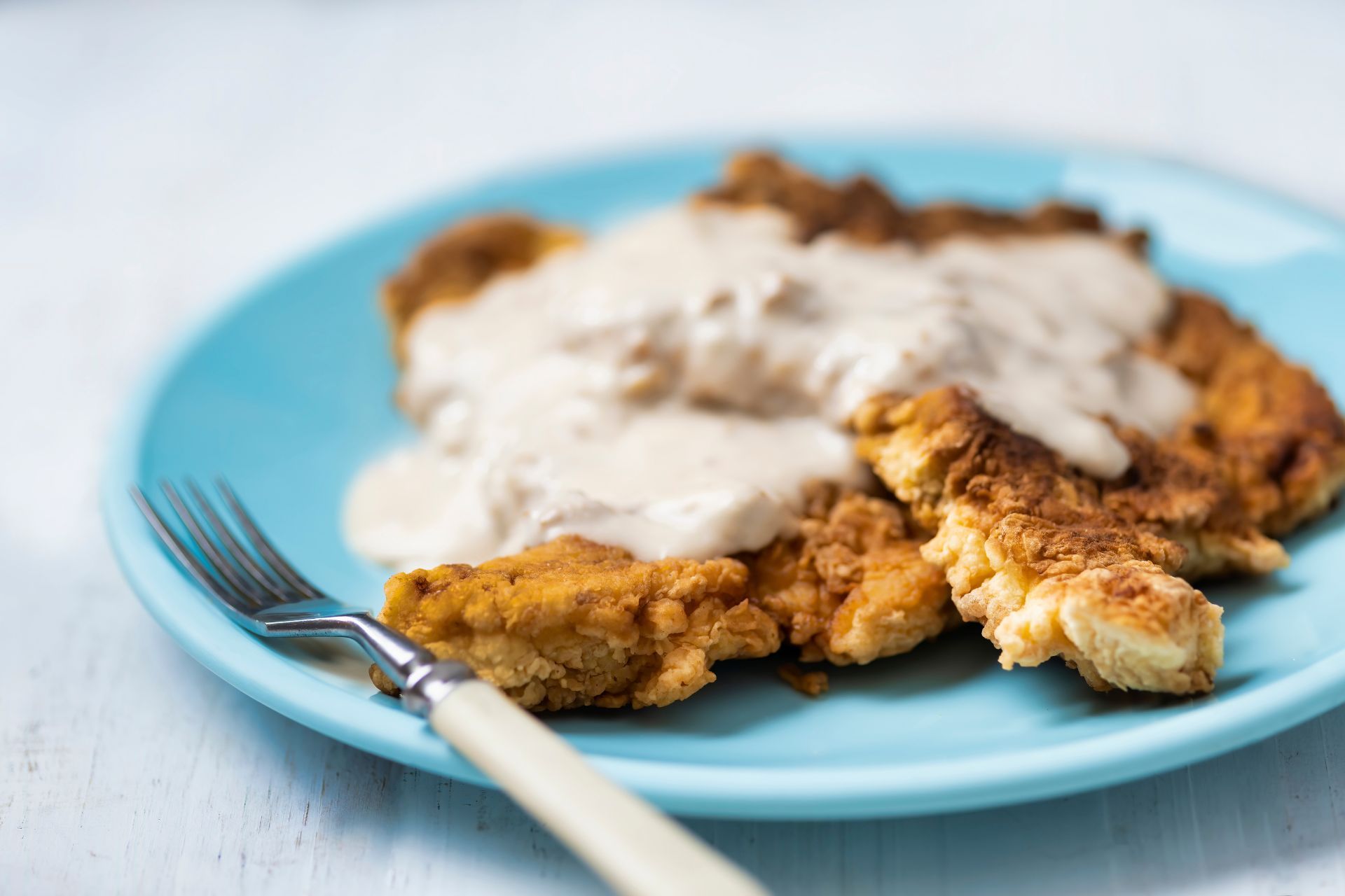 A blue plate topped with fried chicken and gravy with a fork.