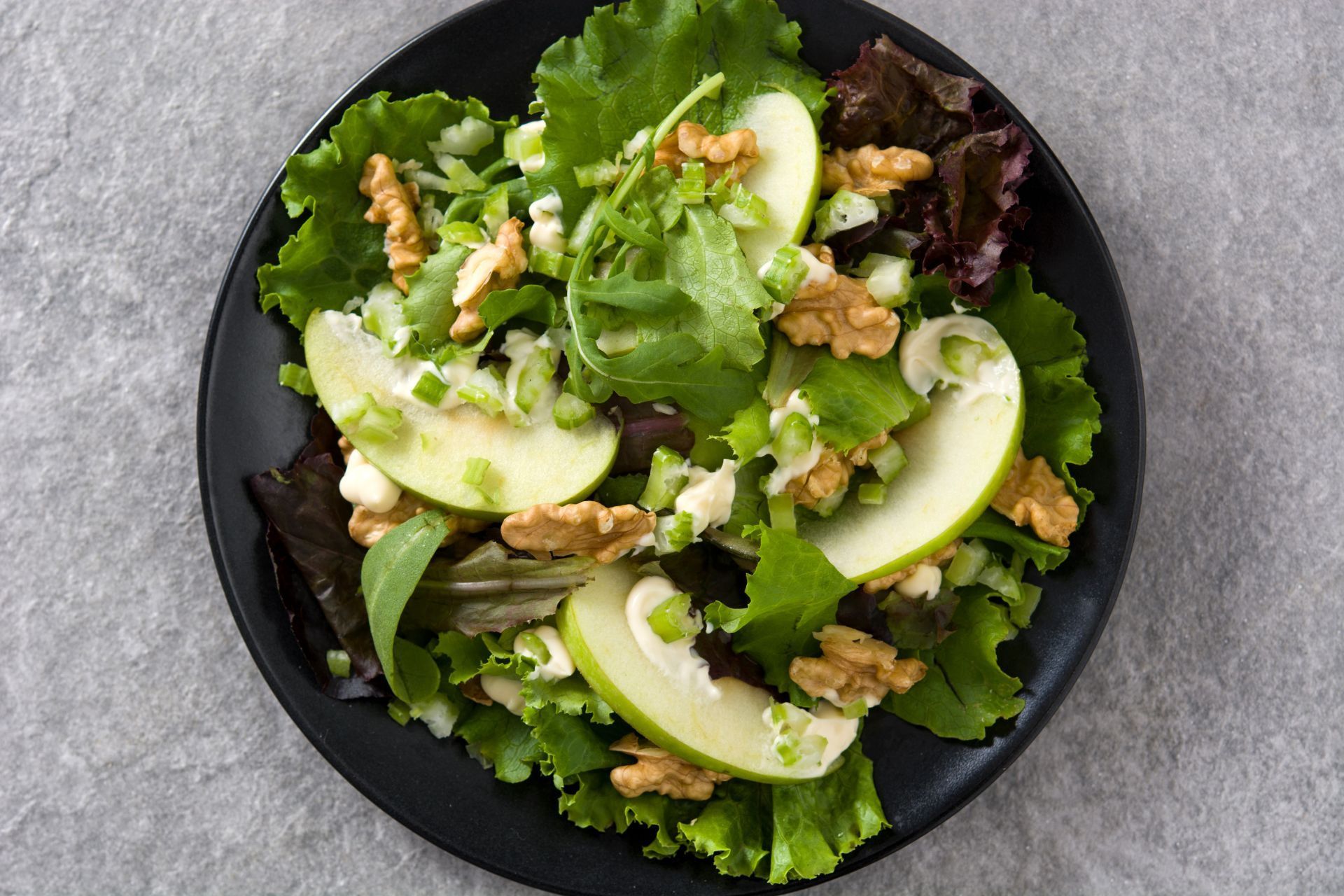 A salad with apples , lettuce , walnuts and onions on a black plate.