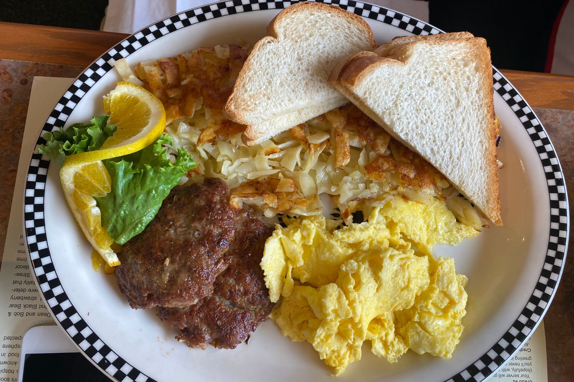 A plate of food with eggs , meat , hash browns and a slice of bread