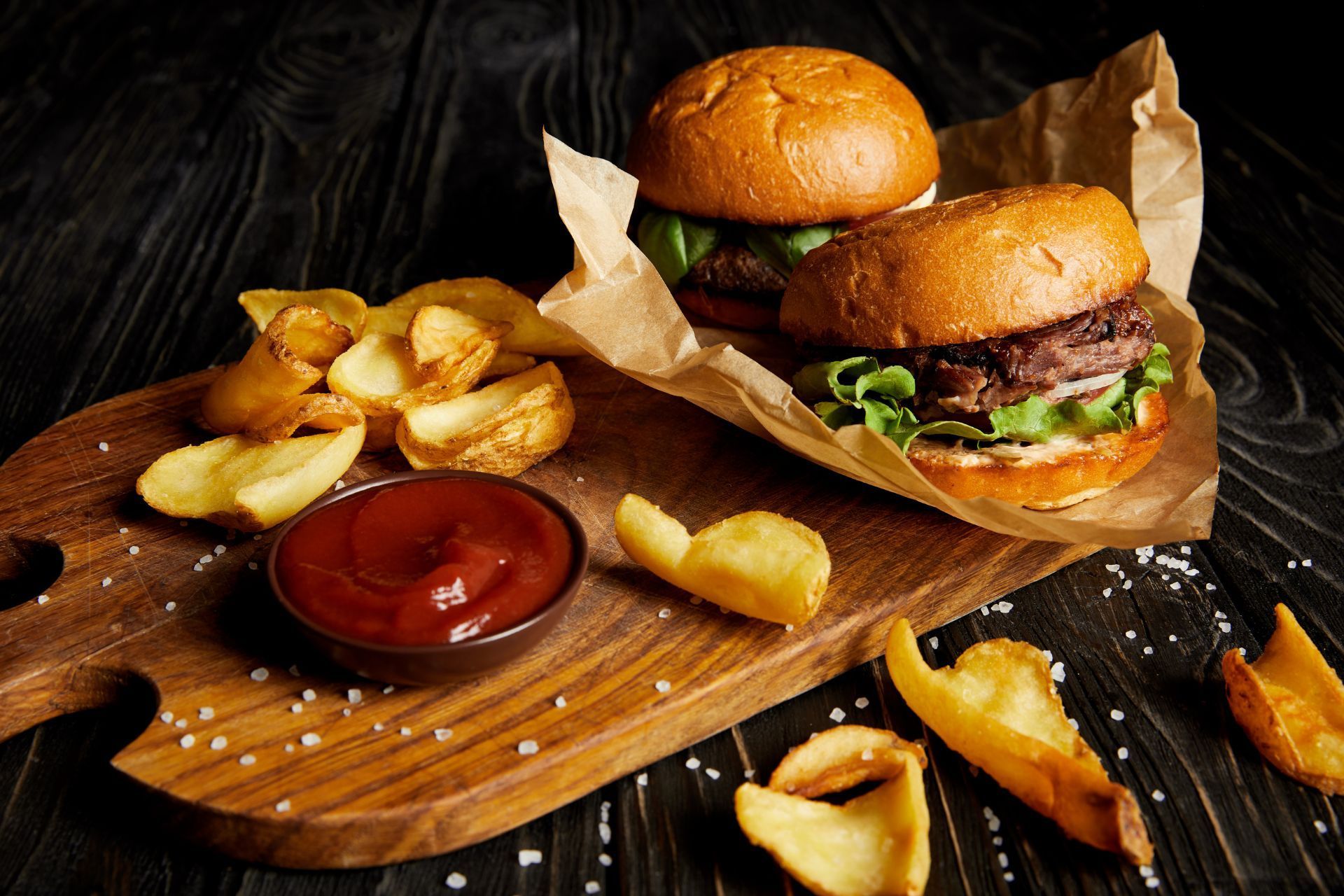 Two hamburgers and french fries on a wooden cutting board.