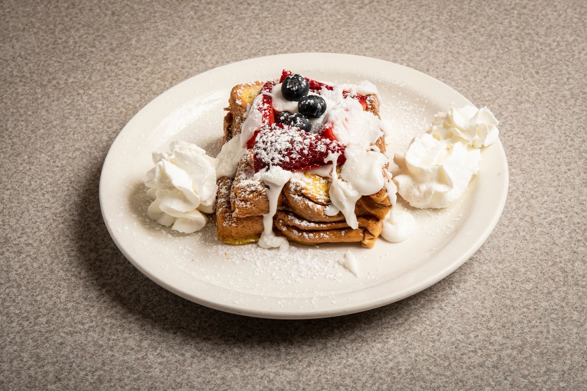 A white plate topped with french toast with whipped cream and berries.
