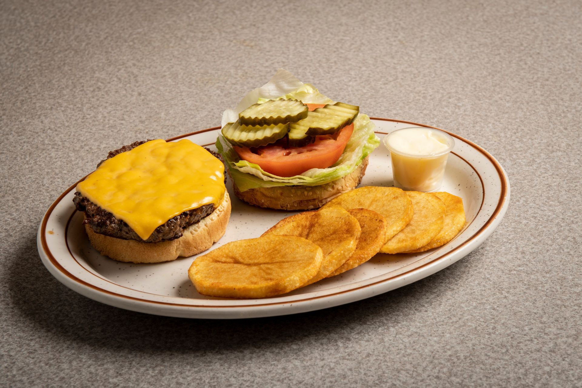 A hamburger with cheese , lettuce , tomato , pickles and french fries on a plate.