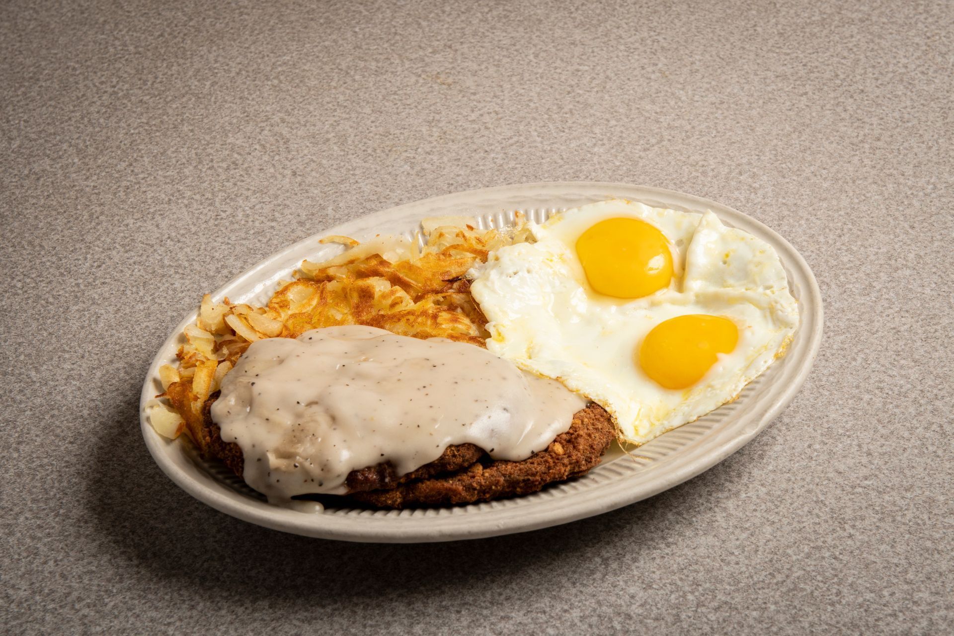 A plate of food with eggs , gravy and hash browns on a table.